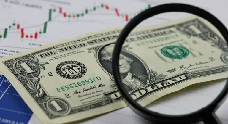 Magnifying glass on US dollar bill with interest rate graph, symbolizing Federal Reserve impact.